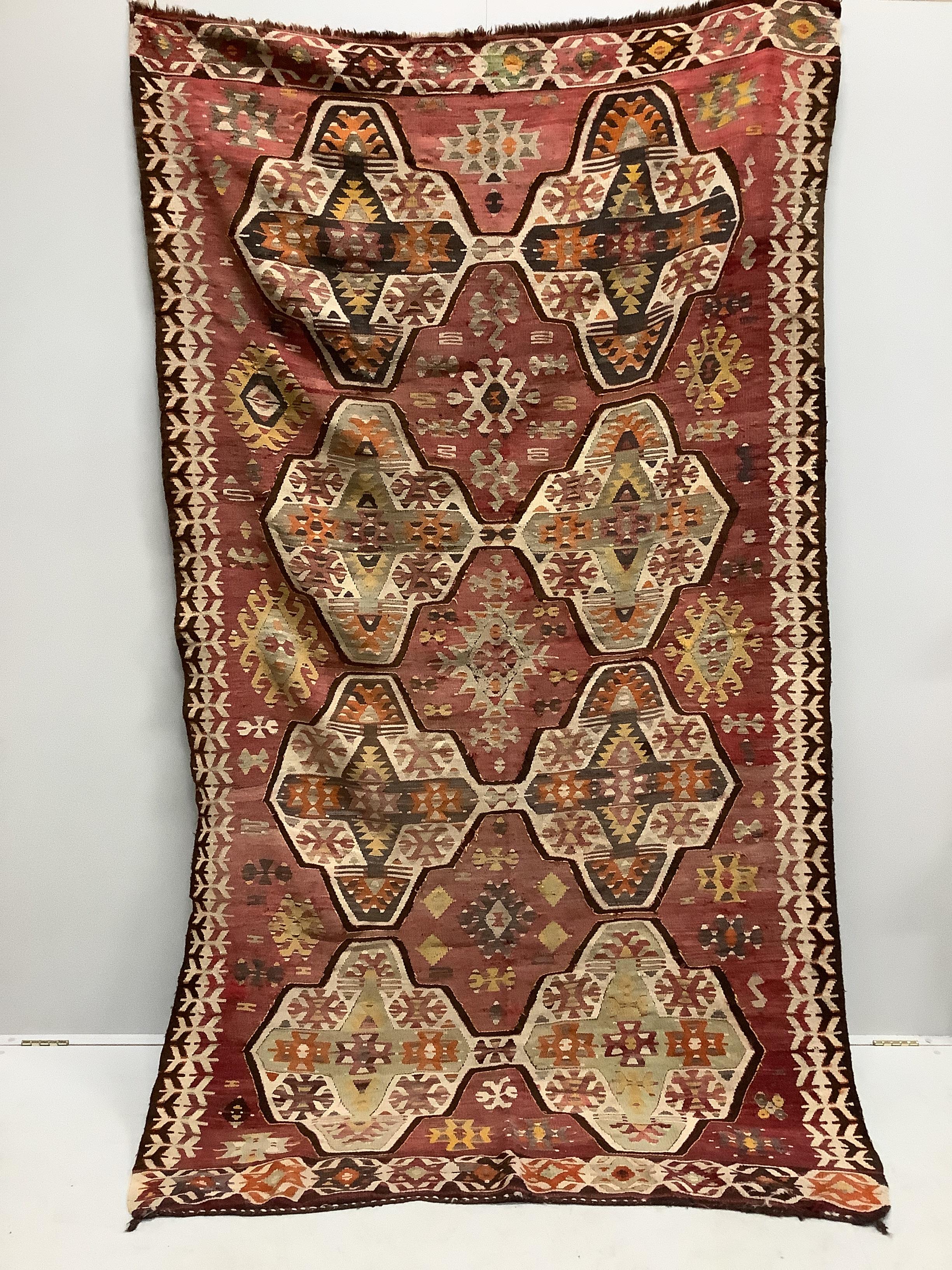 An antique Anatolian Kilim carpet woven eight octagonal medallions on a brick red ground, 266cm x 153cm